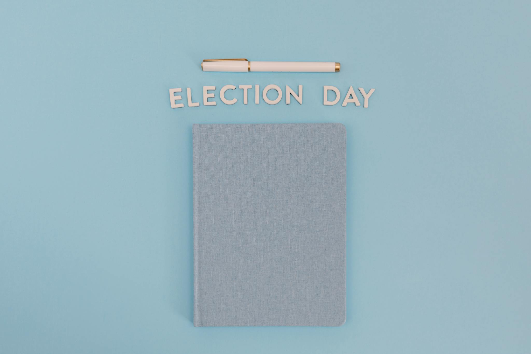 Flat lay of a notebook and pen with 'Election Day' text on a blue background.